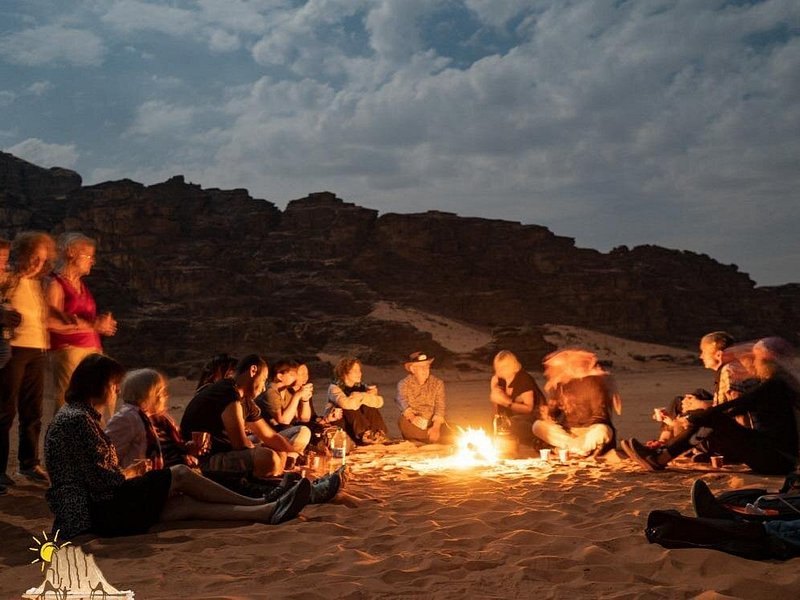 A campfire burning at a Wadi Rum camp after dark, figures around it in silhouette