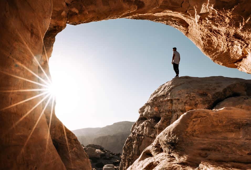 A walker silhouetted under a natural rock arch in Wadi Rum